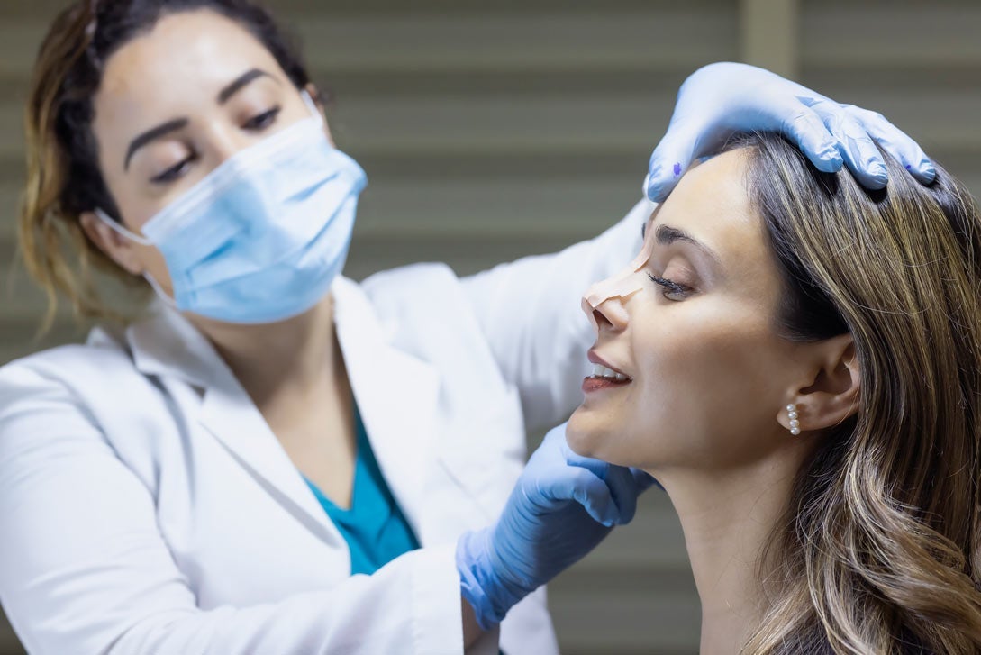 A doctor places tape on a woman's nose to simulate a rhinoplasty (surgery) 