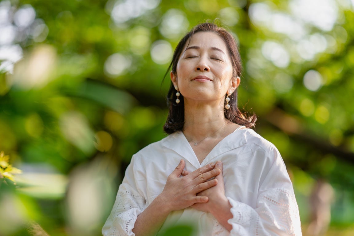 Woman holding chest and breathing outdoors